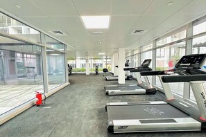 Une salle de sport équipée de tapis de course, de vélos d’exercice et d’un extincteur.