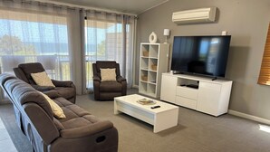 Una sala de estar moderna con un sofá modular, dos sillones, una mesa de centro, un televisor sobre un mueble blanco y una estantería.