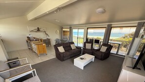 Amplia sala de estar con un conjunto de sofás, una mesa de centro y un mueble para la televisión. Hay un balcón con vistas al mar.