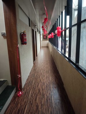 A hallway with a patterned wooden floor, a fire extinguisher mounted on the wall, and red decorations hanging from the ceiling. - Sejal Wolrd Lodging (Koregaon)