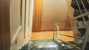 A staircase with wooden steps leading to a landing, a metal handrail, and a wooden wall with vertical slats.