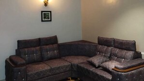 A corner living room with a dark brown sectional sofa, a framed picture on the wall, and a ceiling light fixture.
