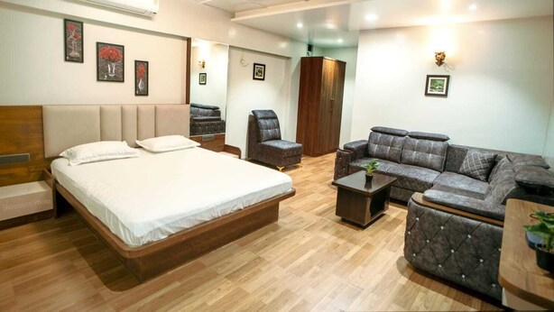 A hotel room with a bed, a sofa, a chair, a small table, and a wardrobe.