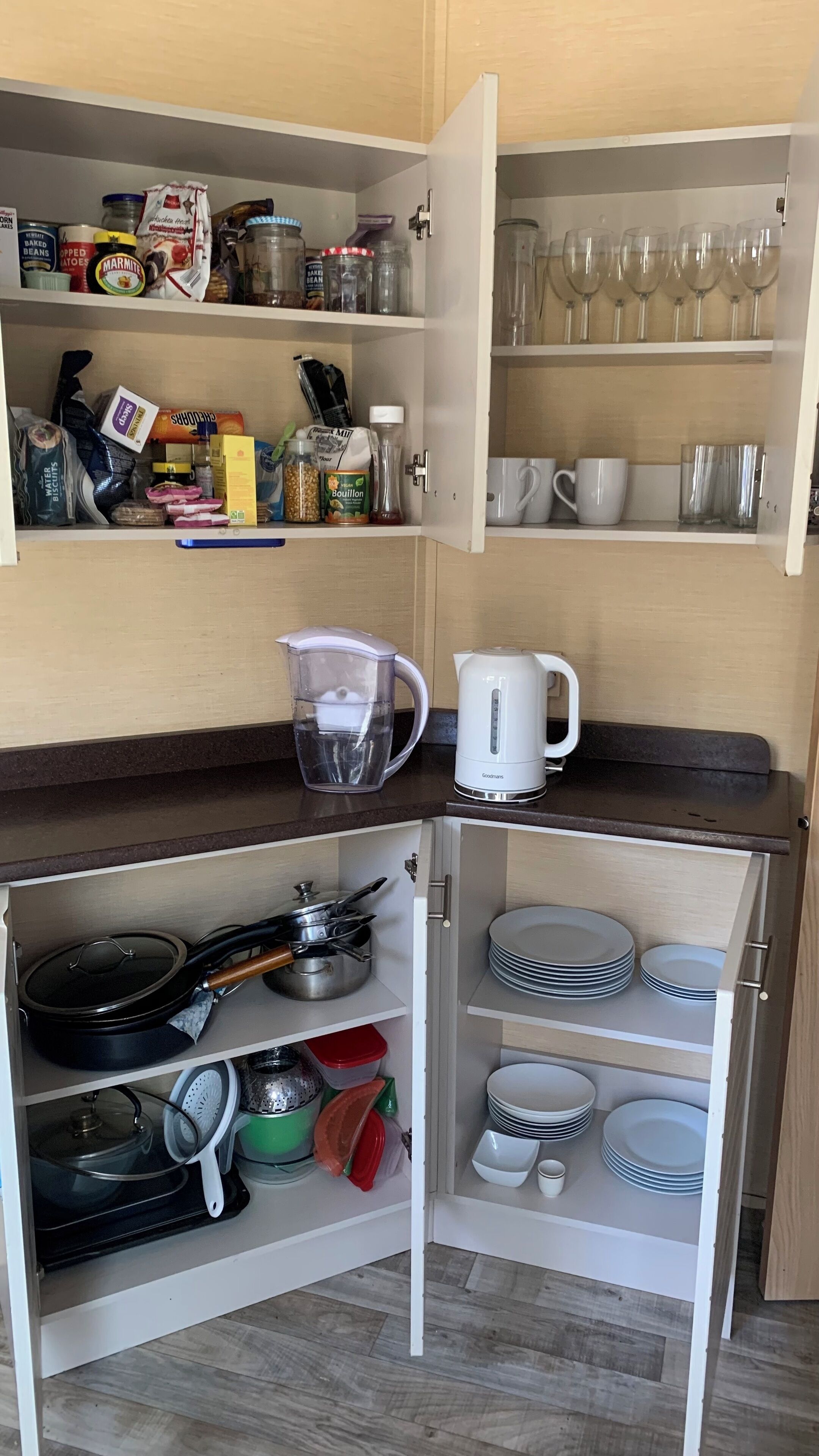 Una cocina con alacenas abiertas que exhiben diferentes alimentos, una tetera y una jarra de agua.