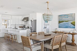 A modern kitchen with white cabinetry, a stainless steel refrigerator, and a dining area with a wooden table and woven chairs.