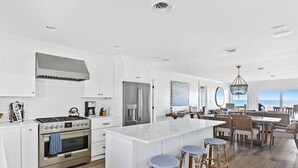 Une cuisine spacieuse avec des meubles blancs, des appareils en acier inoxydable et un grand îlot central doté de tabourets.