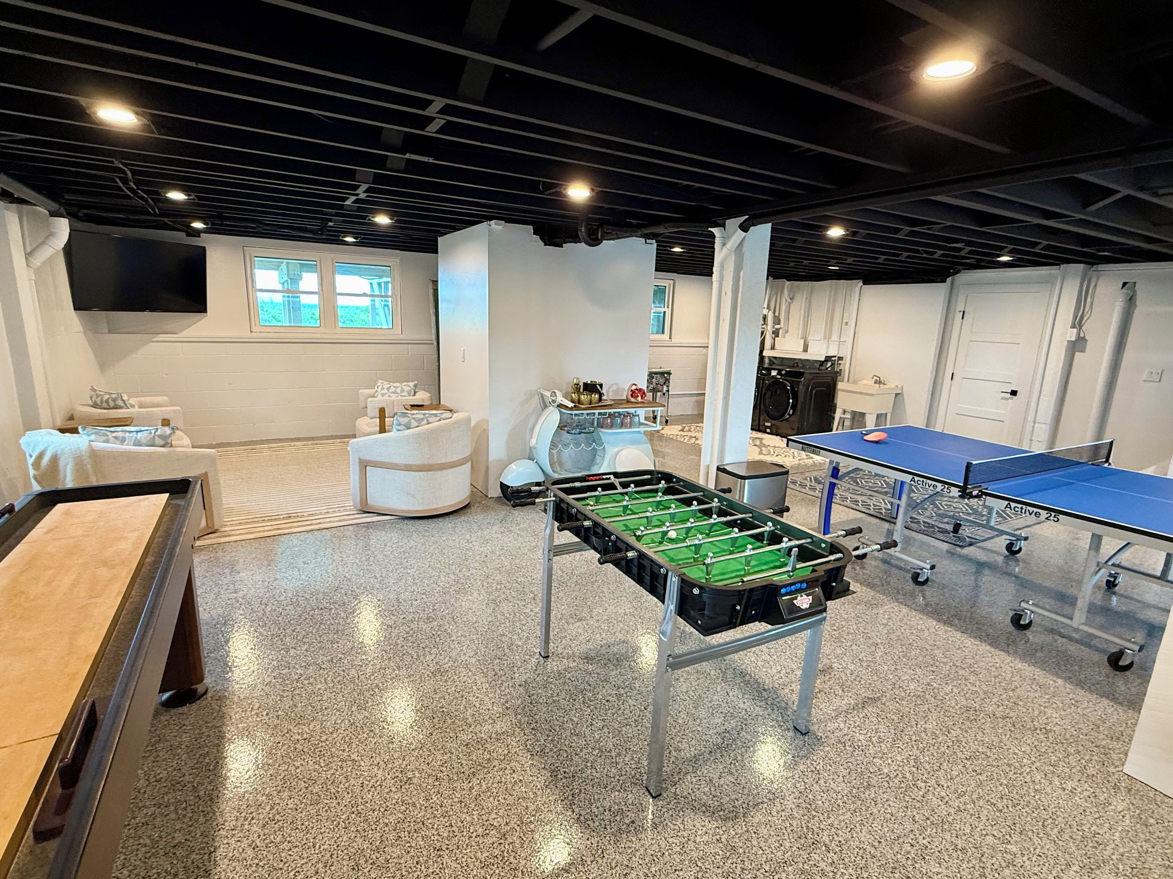 A spacious room with a foosball table, ping pong table, and a sofa.