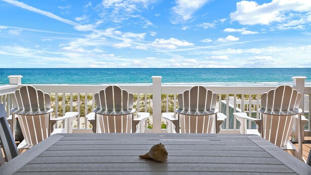 Une terrasse avec des fauteuils Adirondack et une table donnant sur une plage.
