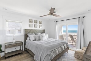 A bedroom with a bed, a ceiling fan, a window, and a view of the beach.