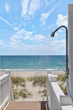 A beach view with a pathway leading to the ocean, a white fence, and a metal lamp post.