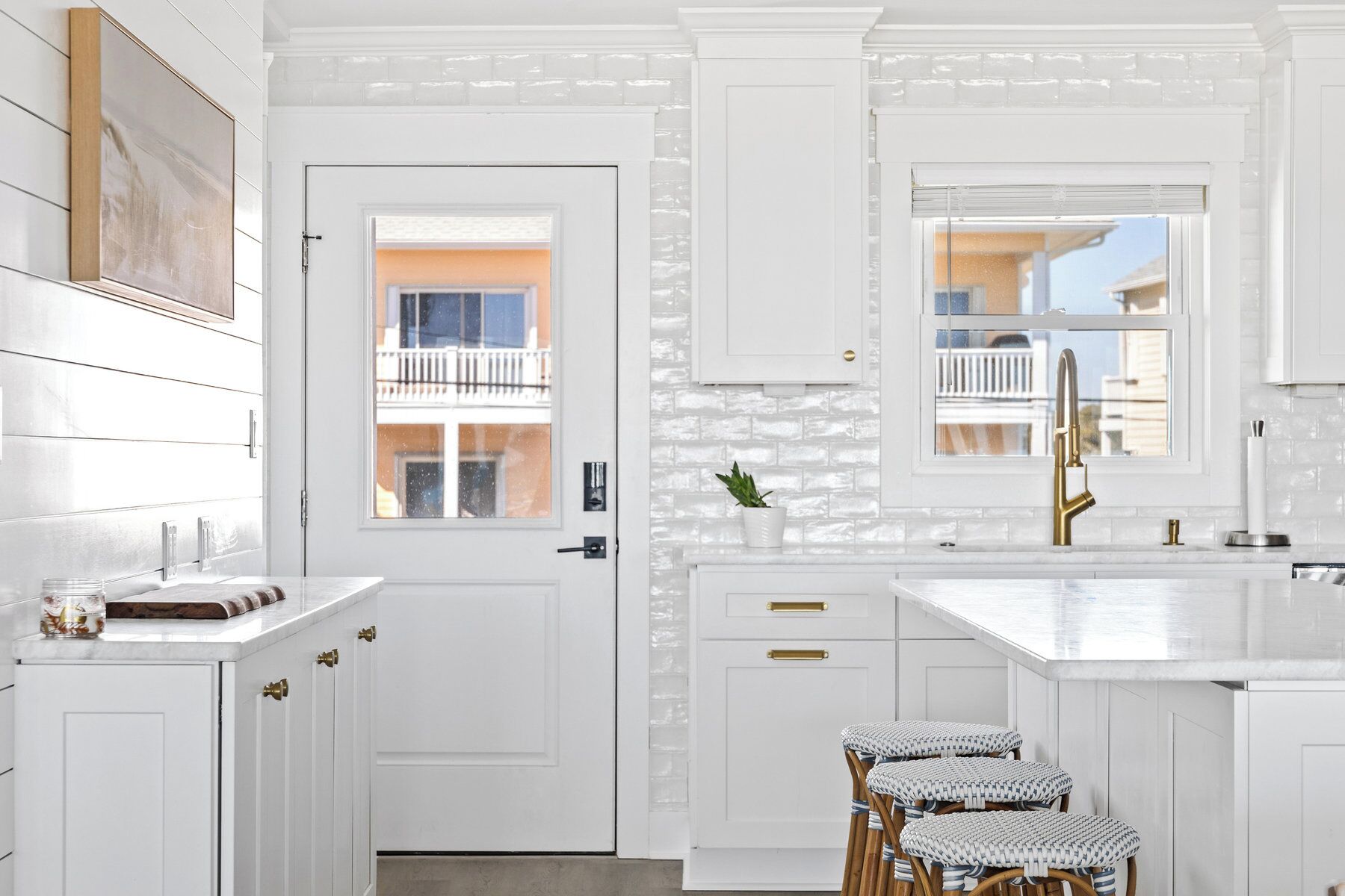 A modern kitchen with white cabinetry, a large window, and a built-in island with stools.