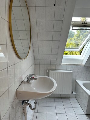 Sink and mirror set against white tiled walls, with a window offering a view of lush greenery.