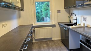 A modern kitchen with a window, built-in appliances, and a view of greenery outside. - Elbnahes Juwel in Hamburg Wedel (Wedel)