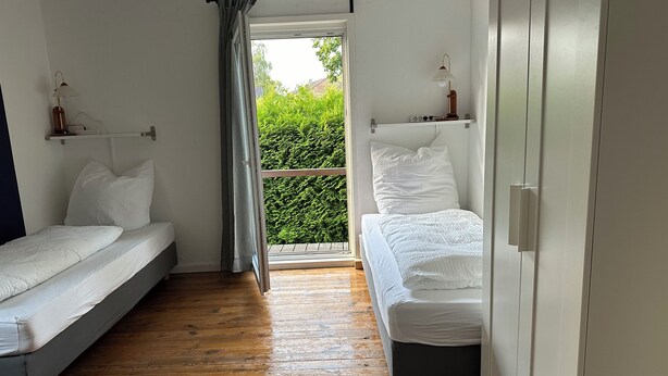 A bedroom with two beds, wooden flooring, and a balcony with greenery. - Elbnahes Juwel in Hamburg Wedel (Wedel)