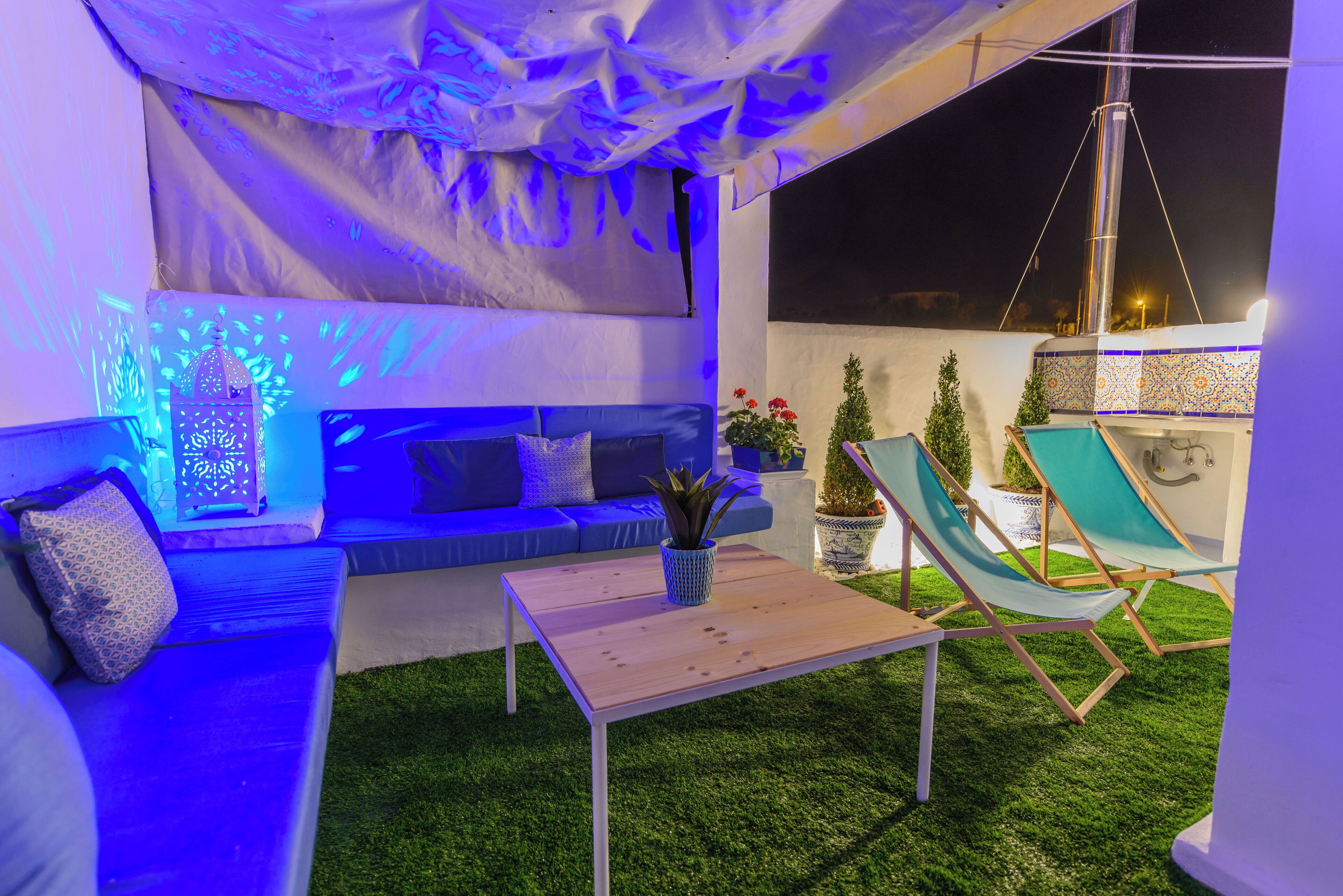 An outdoor seating area with a blue sofa, a wooden table, and two green lounge chairs.