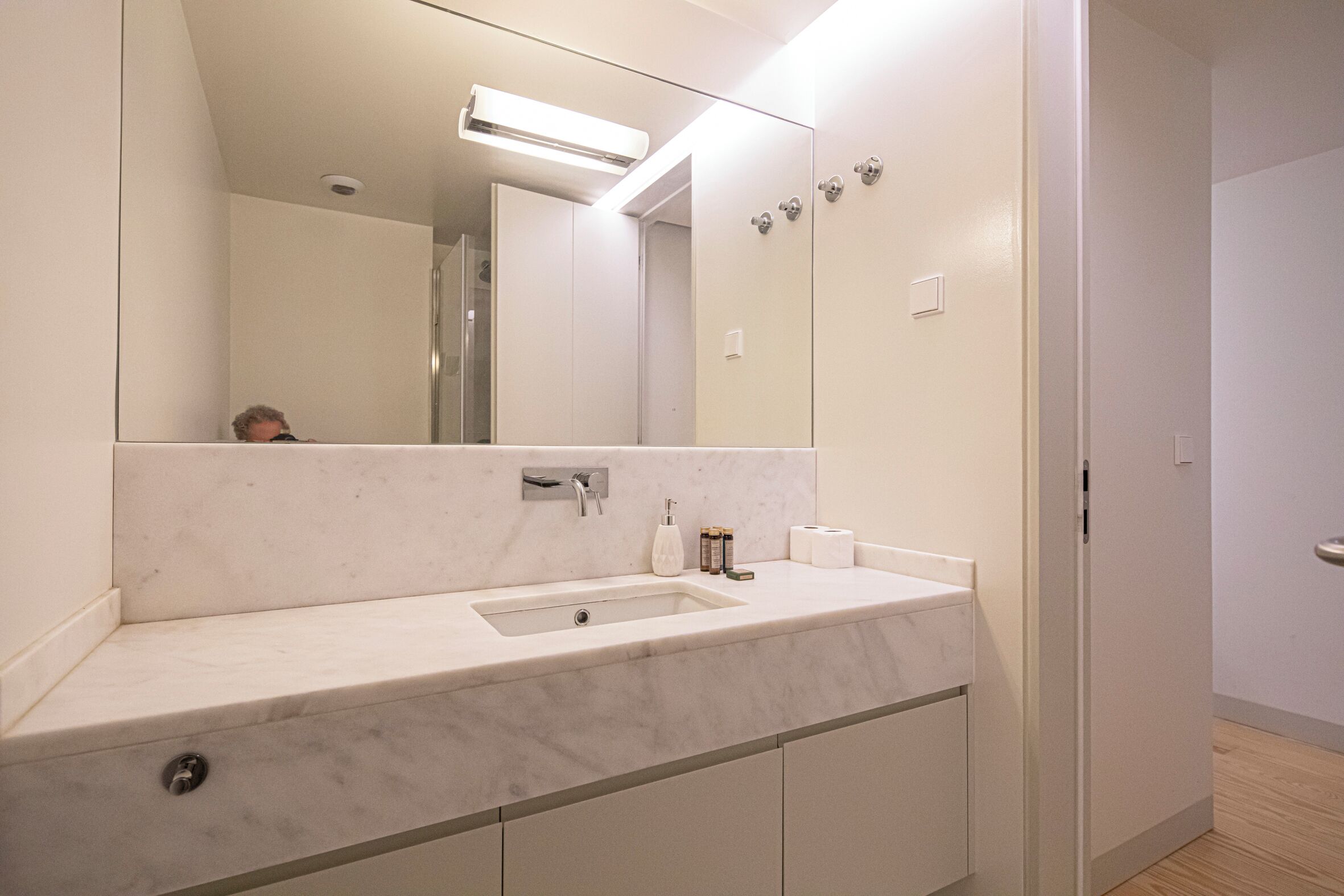Un baño moderno con lavamanos de mármol, un espejo grande y una ducha a ras de suelo.