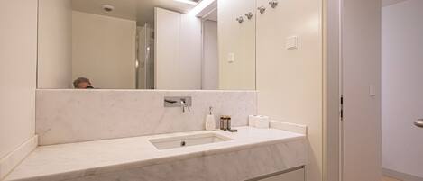 Un baño moderno con lavamanos de mármol, un espejo grande y una ducha a ras de suelo.