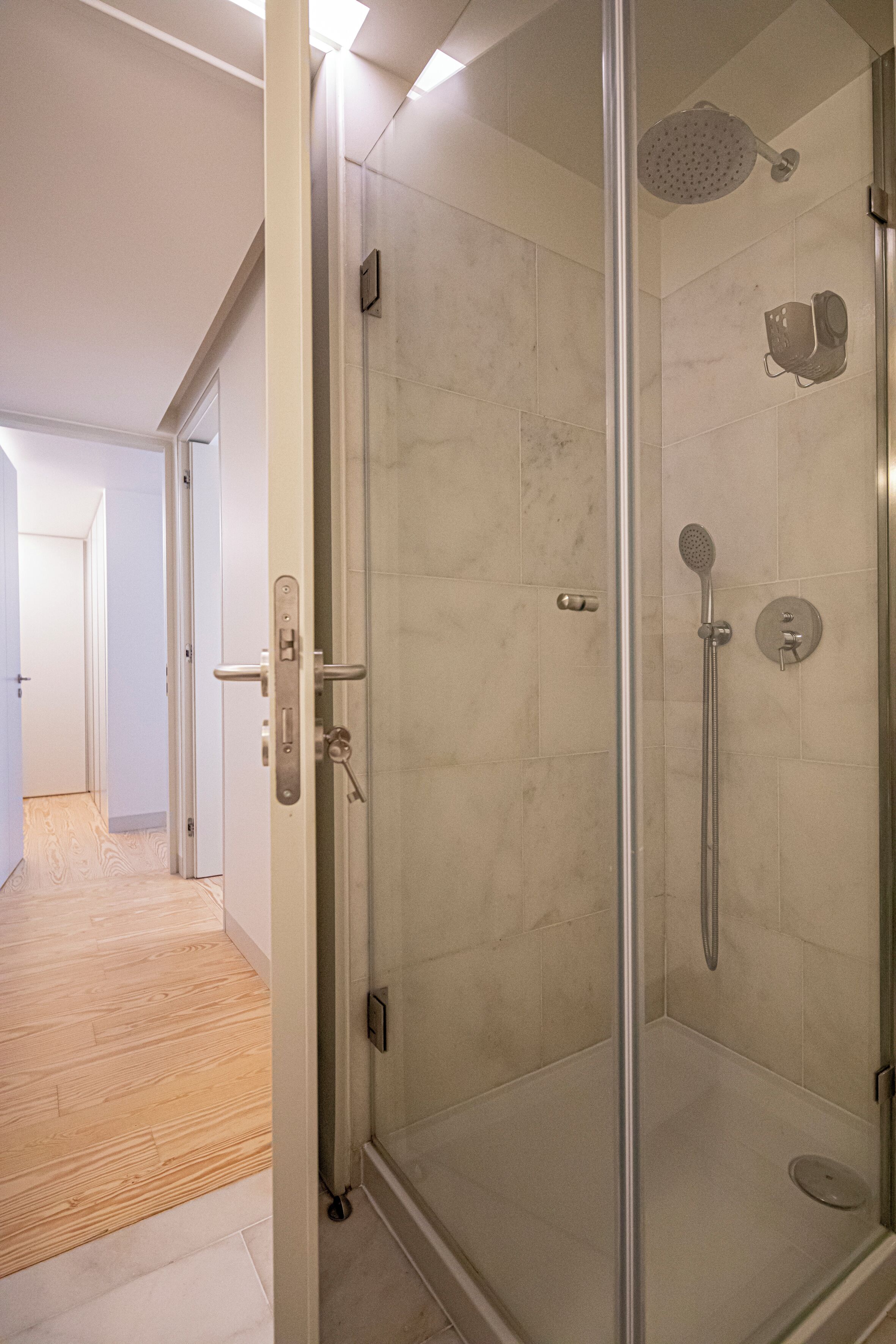 A modern bathroom with a glass-enclosed shower, a handheld showerhead, and a wall-mounted faucet.
