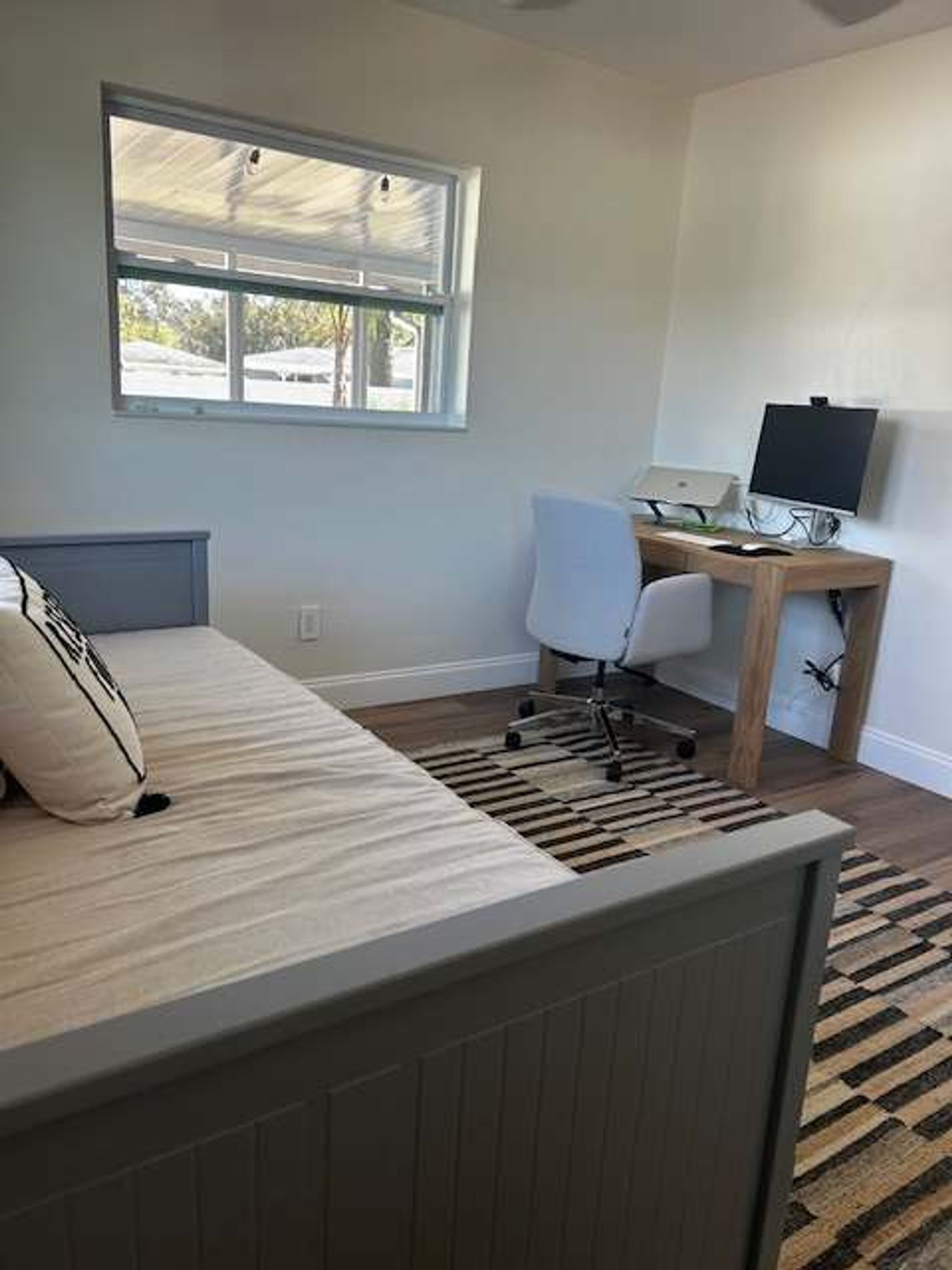 Une chambre à coucher avec un lit, un bureau avec un ordinateur et une fenêtre.