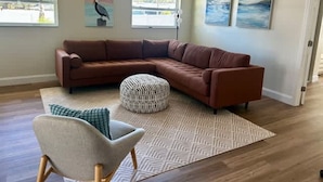 A living room with a brown sectional sofa, a patterned ottoman, a light-colored armchair, and a geometric rug. - NEW Stunning Home-close to Beaches-pet Friendly (Largo)