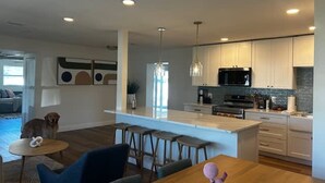 A modern kitchen with white cabinets, a central island, and a dining area with a blue chair and wooden table. - NEW Stunning Home-close to Beaches-pet Friendly (Largo)