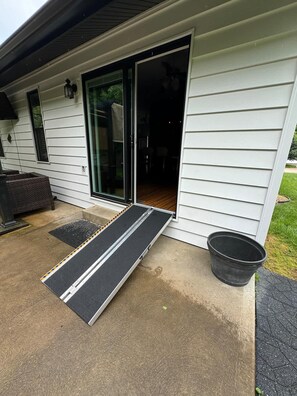 A house with a sliding glass door, a small porch, and a black ramp leading to the door.