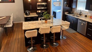 A modern kitchen with dark cabinetry, a marble countertop, and a central island with bar stools. - Remodeled and Inviting Free EV Charging Station Level 2 (Fenton)