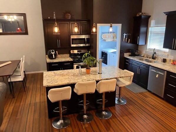 A modern kitchen with dark cabinetry, a marble countertop, and a central island with bar stools.