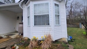 A white house with a bay window, a stone border around the front yard, and a lawn with some plants. - Remodeled and Inviting Free EV Charging Station Level 2 (Fenton)