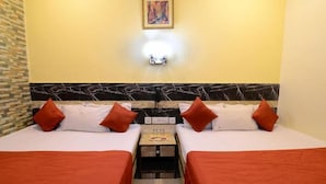 Habitación de hotel con dos camas, cada una con ropa de cama blanca y detalles en naranja, cabecera de mármol y una mesita de noche con lámpara.
