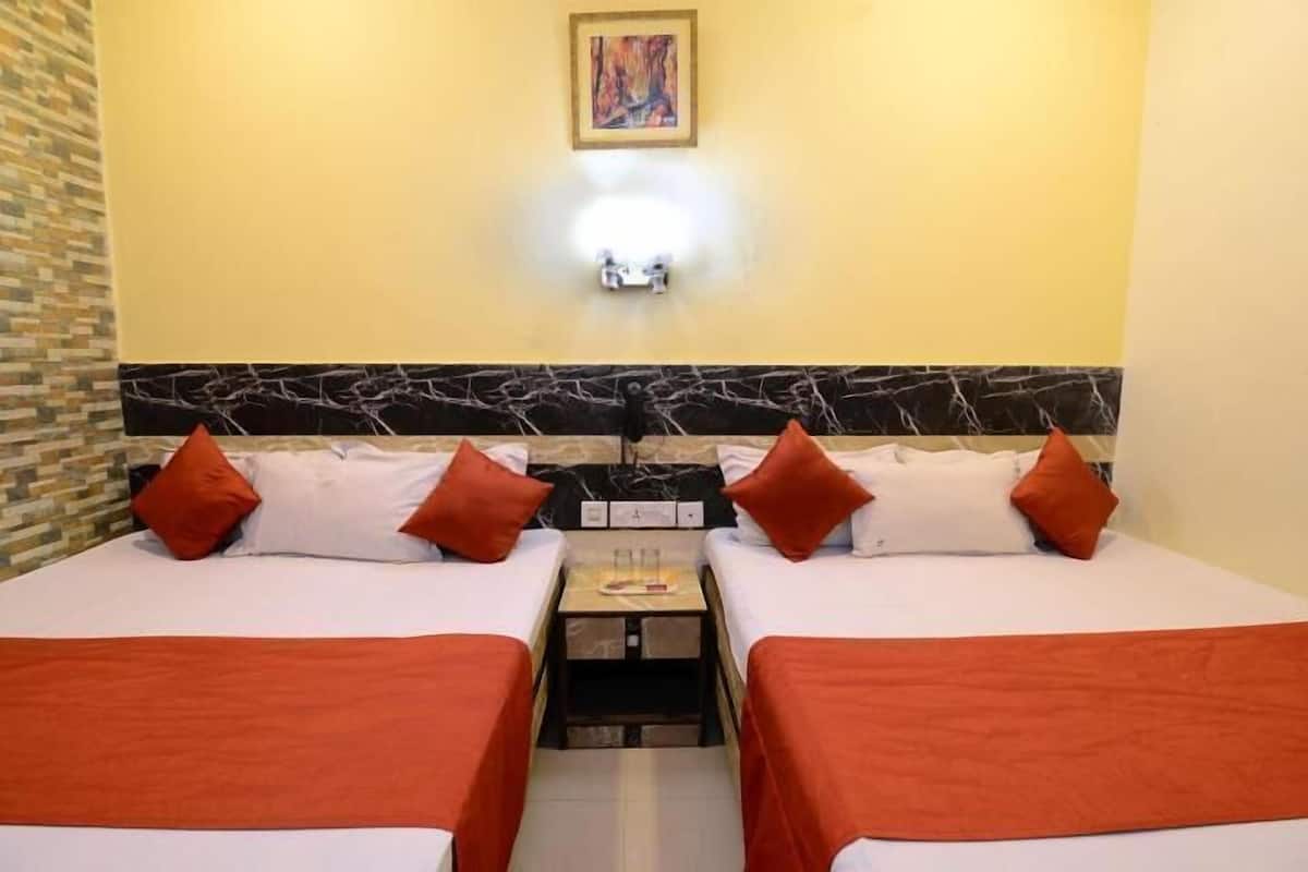 A hotel room with two beds, each with white bedding and orange accents, a marble headboard, and a small bedside table with a lamp.