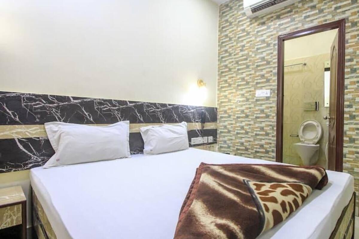 A hotel room with a bed, a headboard with a marble pattern, a bathroom with a toilet and a shower, and a wooden door.