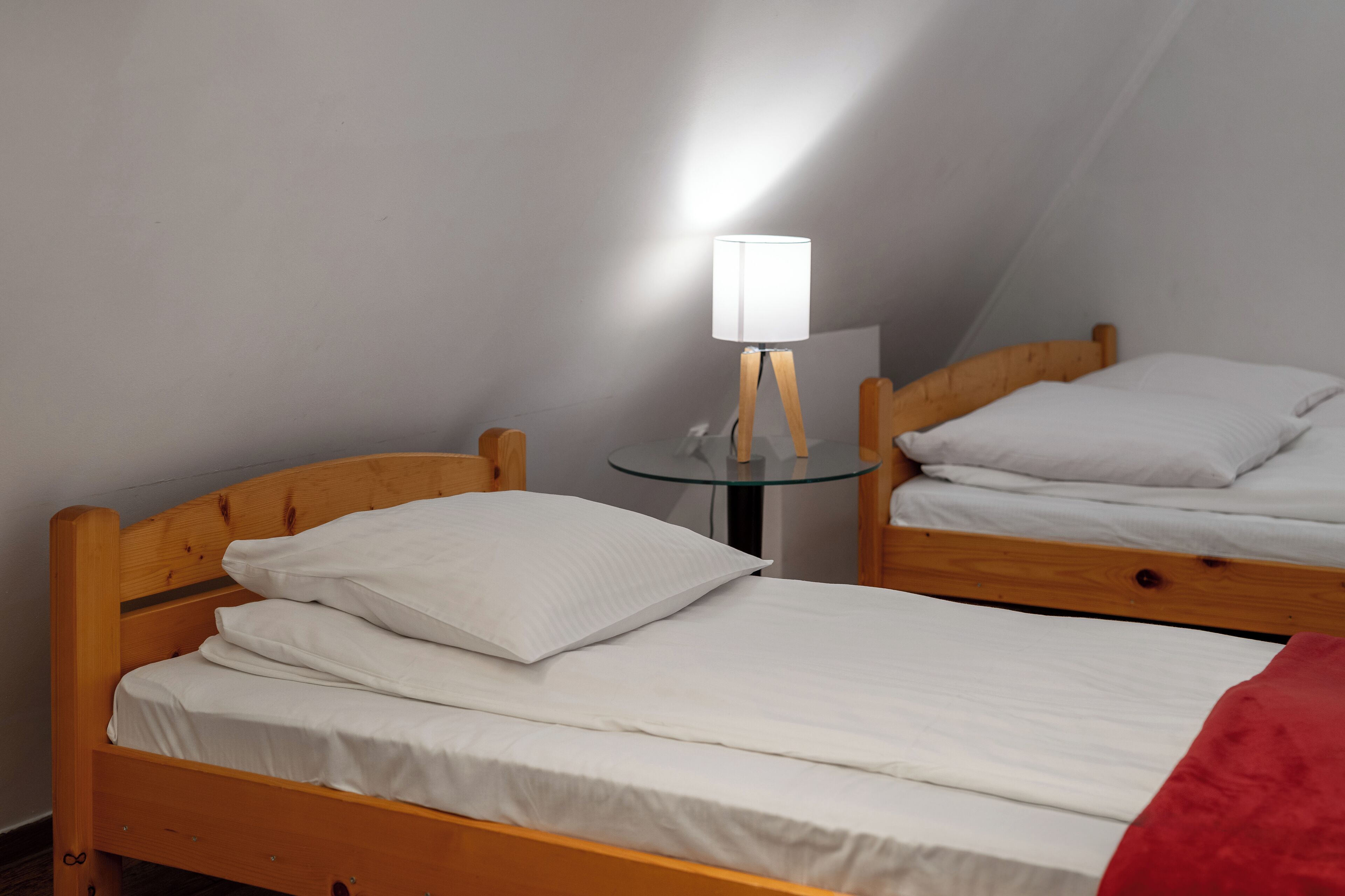 A room with two wooden beds, a glass table with a lamp, and a mirror on the wall.