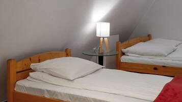 A room with two wooden beds, a glass table with a lamp, and a mirror on the wall.