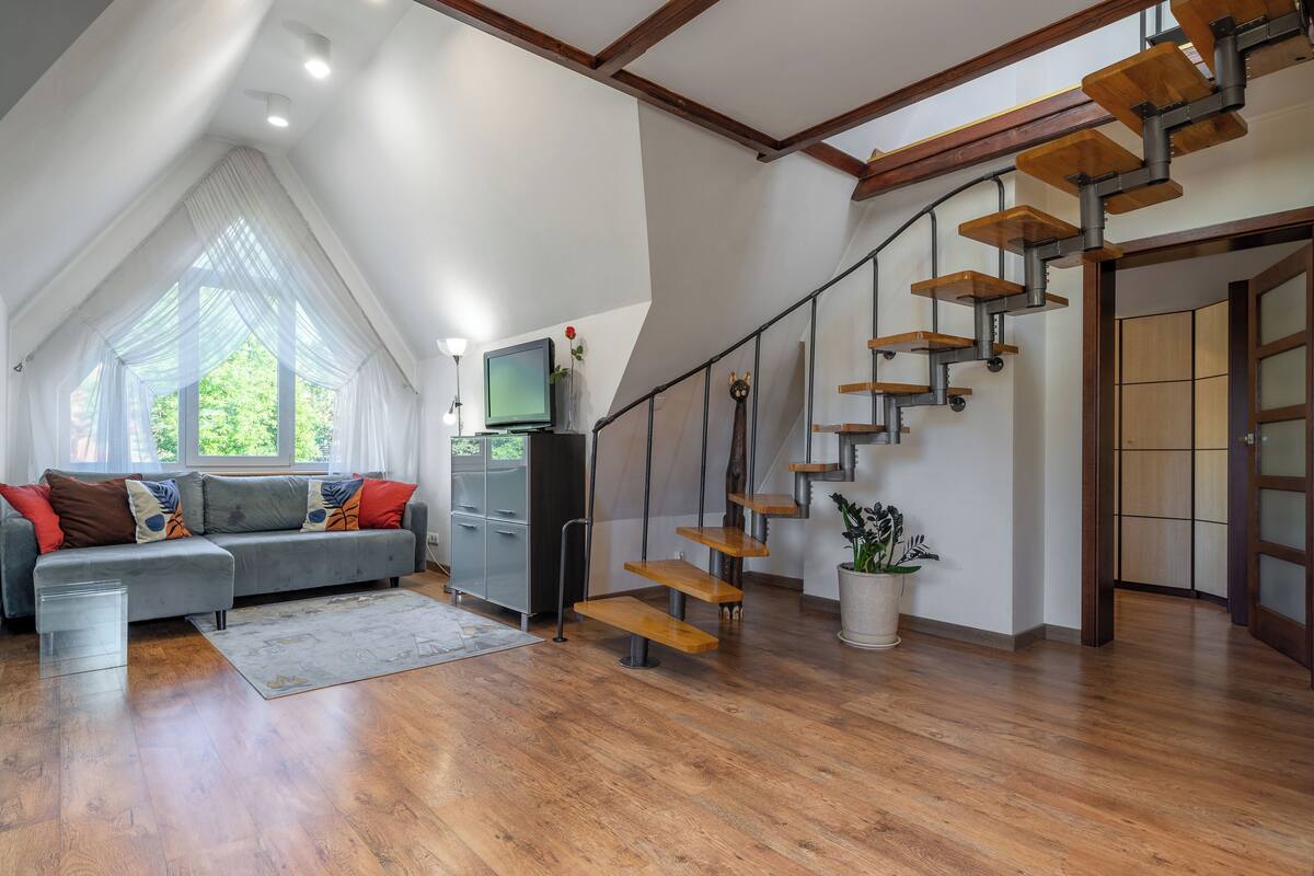 A modern living room with a wooden staircase, a grey sofa, and a flat-screen TV.