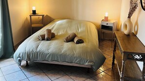 A bedroom with a bed, a bedside table, a nightstand, a wall decoration, and a wooden bench. - Le Cellier Vacation Rental - A Break in the Countryside (Boissay)