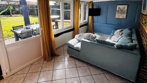 A room with a blue sofa, a dining table, and a view of a garden. - Le Cellier Vacation Rental - A Break in the Countryside (Boissay)