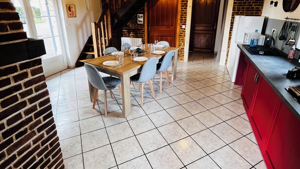 A spacious kitchen with a dining area, featuring exposed wooden beams, a brick wall, and a tiled floor. - Le Cellier Vacation Rental - A Break in the Countryside (Boissay)