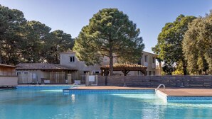 A swimming pool with a wooden deck, surrounded by trees and buildings with tiled roofs. - Apart  with heated pool by Pinarello Villa Services (Lecci)