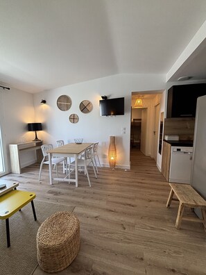 A modern kitchen with a built-in oven, a dining area with a wooden table and chairs, and a TV mounted on the wall.