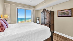 Een slaapkamer met een groot bed, een plafondventilator, een houten garderobe en uitzicht op het strand.