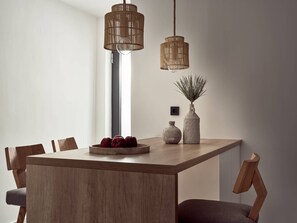 Et moderne spiseområde med et træbord, to hængende fletlamper og en vase med en plante.