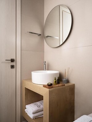 Un baño moderno con un espejo redondo, un lavabo blanco y un mueble de tocador de madera.