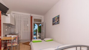 Habitación de hotel pequeña con cama, un escritorio con silla, televisión y vista al mar por una puerta abierta.