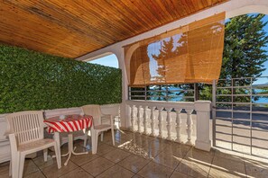 Een overdekt terras met een tafel en stoelen, een uitzicht op zee en een groene haag.