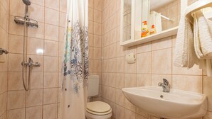 Un baño con ducha, inodoro, lavabo y un estante con artículos de aseo.