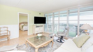 Un salon comprenant un téléviseur, un canapé, un fauteuil, une table basse et de grandes fenêtres offrant une vue dégagée.