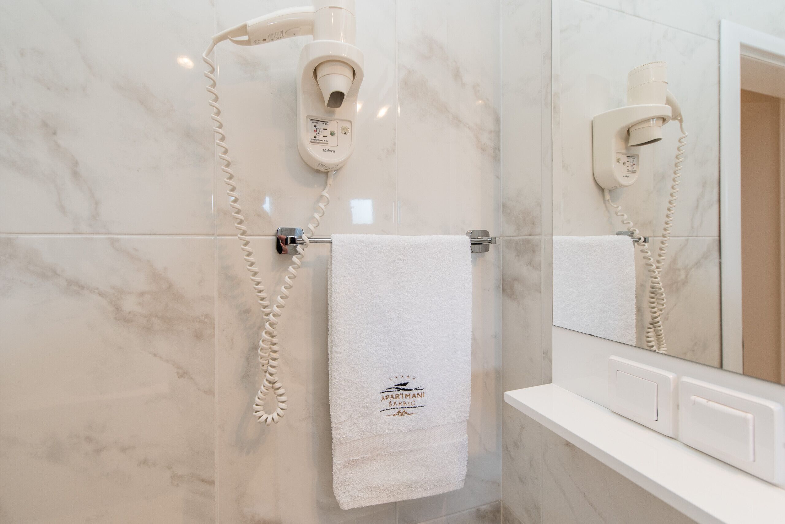 A bathroom with a marble wall, a white towel hanging on a rack, and a hairdryer mounted on the wall.