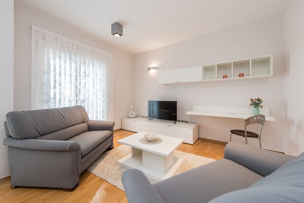 Una sala de estar moderna con un sofá gris, una mesa de centro blanca y un televisor sobre un mueble blanco.