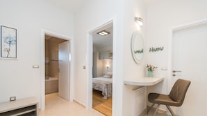 Camera d'albergo moderna con un letto, una scrivania e una sedia. Si intravede un bagno con doccia e WC attraverso una porta aperta.